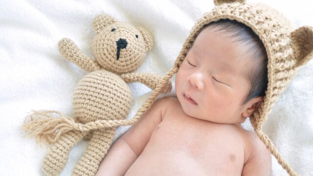 クマのぬいぐるみと一緒に眠るクマ帽子をかぶった赤ちゃん